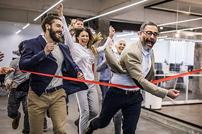 Large group of business people having fun while crossing the finish line at casual office. Focus is on young bearded man.